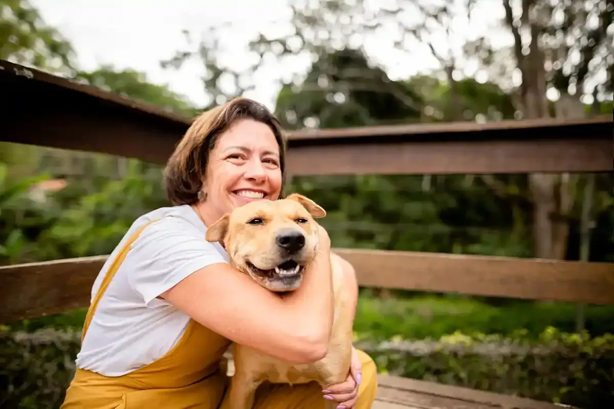 Woman hugging a happy dog on a wooden fence in a green outdoor setting