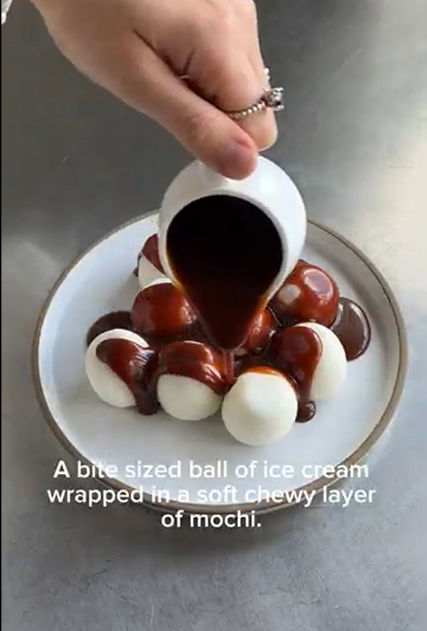 Chocolate sauce being poured over white, round mochi ice cream balls on a plate.