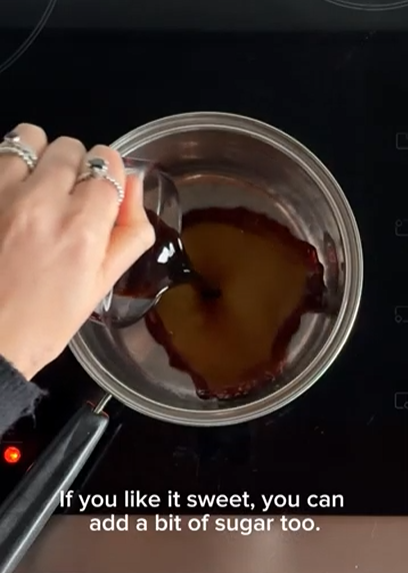 A hand pours a dark liquid from a glass into a silver saucepan on a stovetop with the text, 