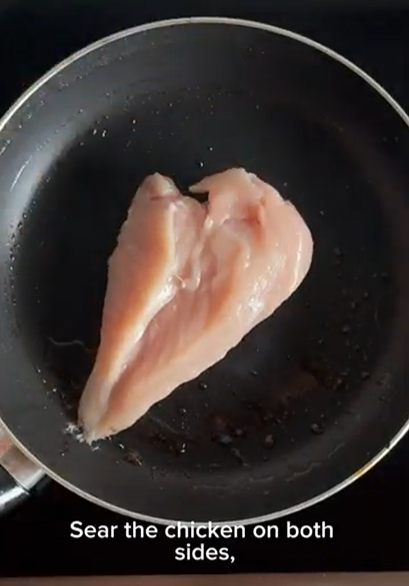 Raw chicken breast searing in a dark non-stick frying pan, with the text overlay 