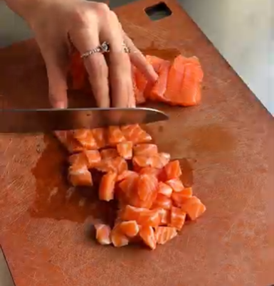 Hand chopping salmon on a wooden cutting board