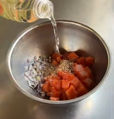 Oil being poured into a bowl of chopped tomatoes, onions, and spices on a metal countertop