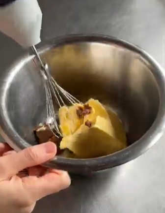 Hand whisking a yellow mixture in a metal bowl, with a hand holding the bowl steady