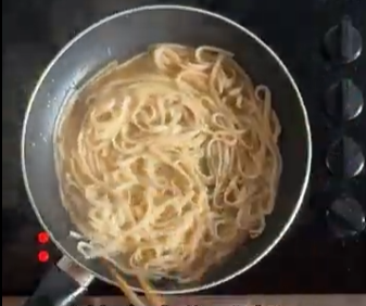 Top-down view of noodles simmering in a black skillet on a stovetop.