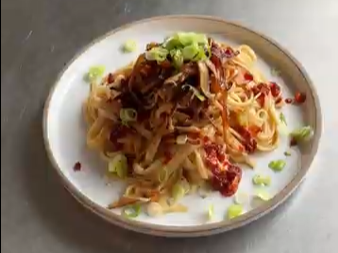 Pasta topped with meat sauce and chopped green onions on a white plate