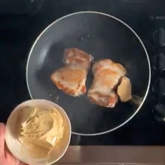 Pan with cooking meat on a stovetop, with a bowl of sliced potatoes in the foreground