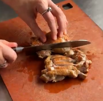 Hands slicing cooked meat on a wooden cutting board