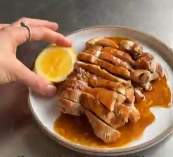 Plate of sliced roasted meat with orange sauce, held with a lemon wedge on the side