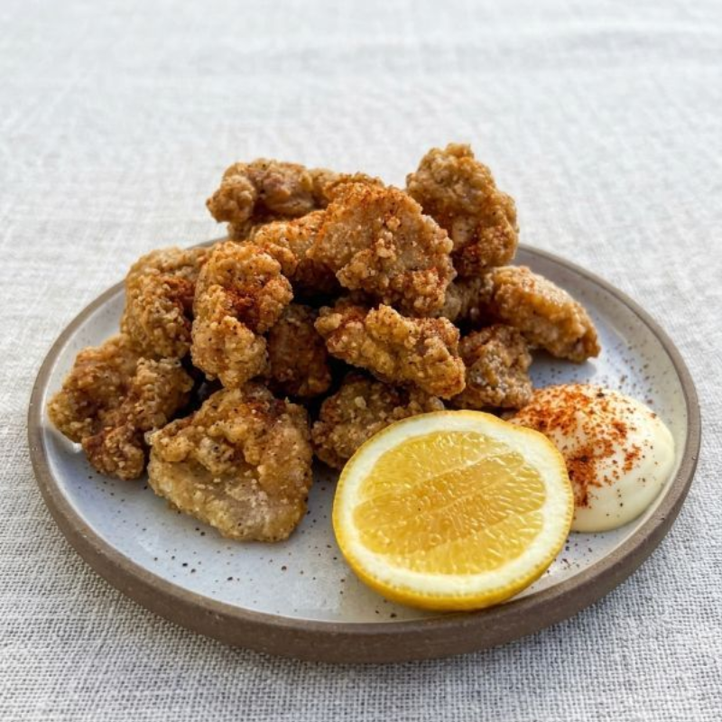 Plate of fried chicken bites with lemon wedge and dipping sauce on a light tablecloth