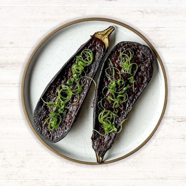 Two roasted eggplants topped with green herbs on a white plate