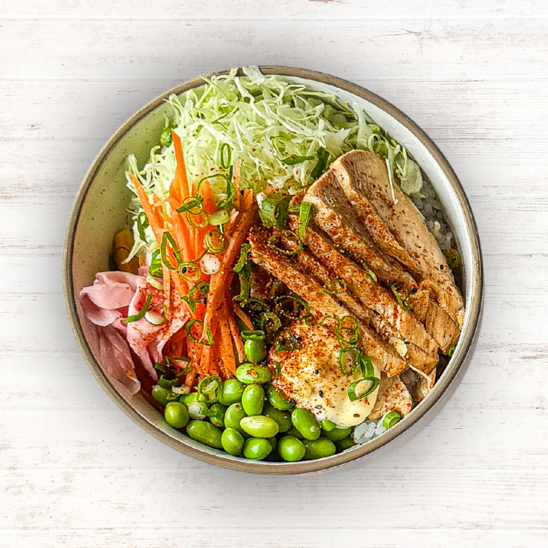 A bowl of chicken teriyaki with edamame, shredded cabbage, sliced carrots, pickled ginger, and rice, seen from above.
