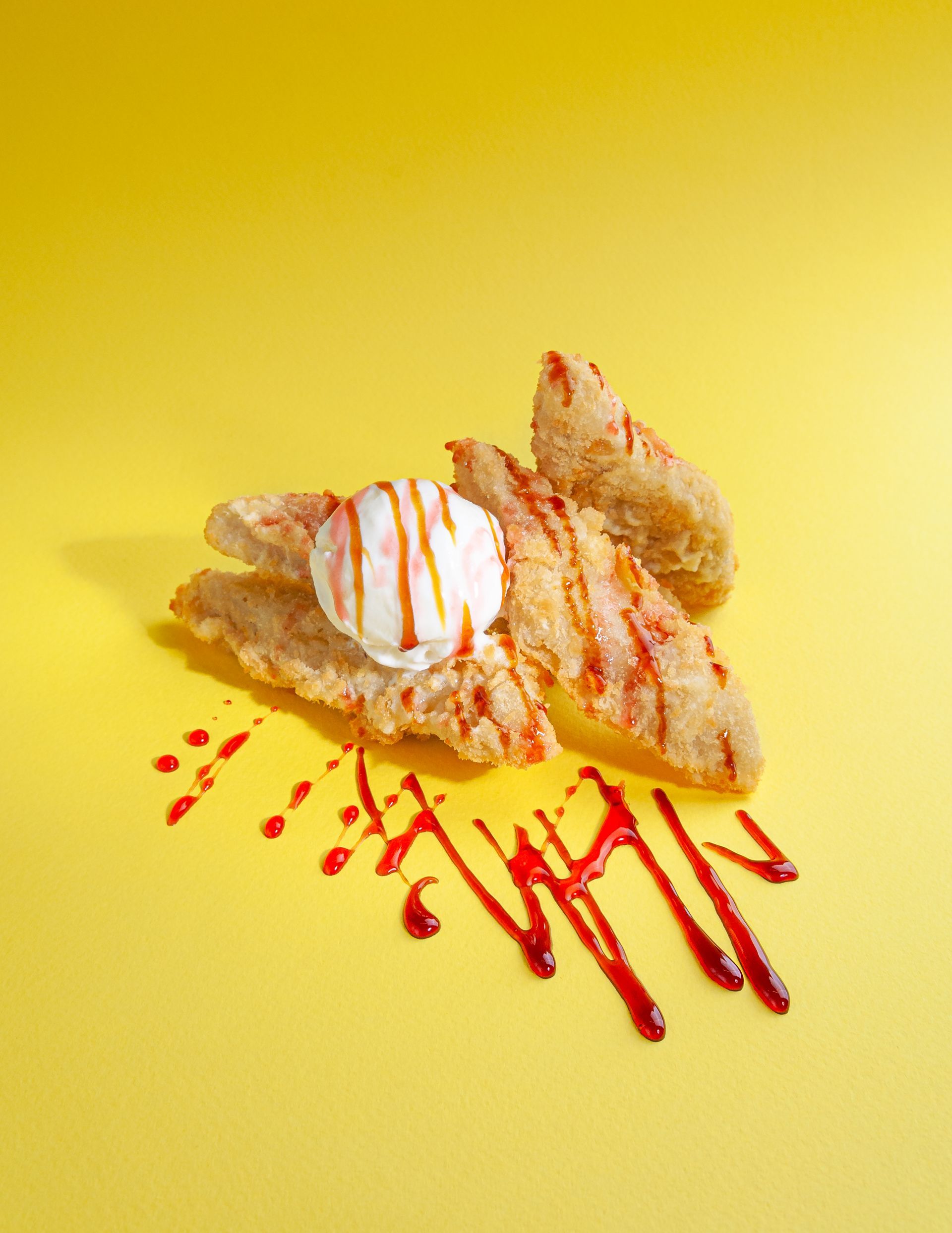 Fried dessert with ice cream and red sauce on a yellow background.