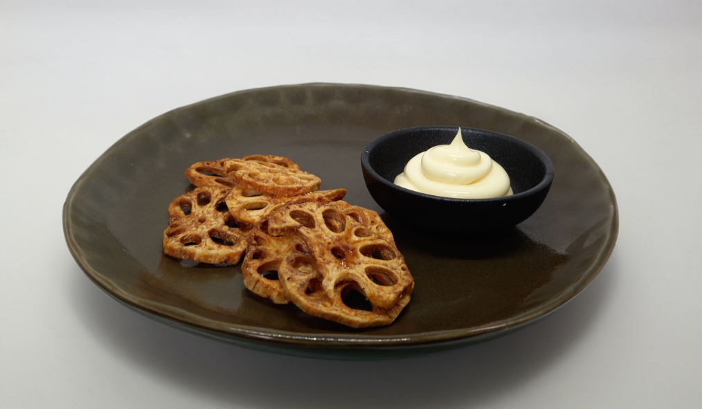 Lotus root chips with creamy dip on a dark plate.
