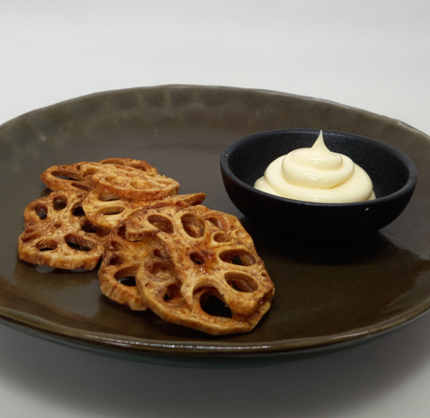 Brown lotus root chips with a small bowl of white dipping sauce on a brown plate.