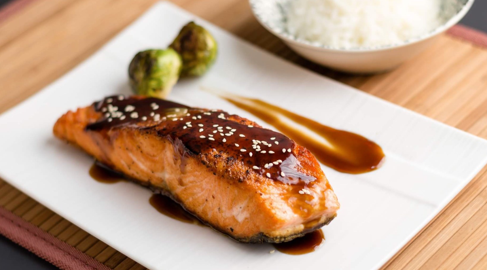 Salmon fillet with glaze, brussels sprouts, and rice on a white plate.
