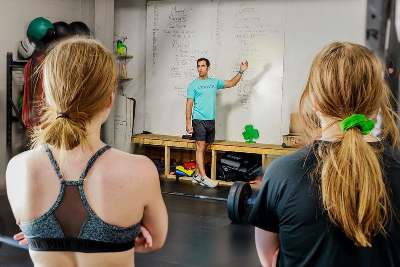 Group of eight people in matching dark shirts posing together indoors against a brick wall at CrossFit Iron Shamrock.