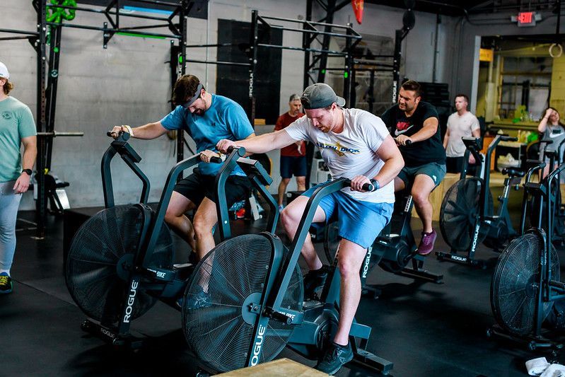 People exercising on fan bikes in a gym in Winter Park, FL with one man in a gray shirt leading the group.