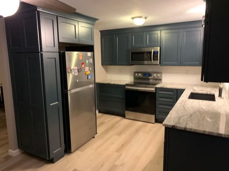 Blue kitchen cabinets and stainless steel appliances in a bright kitchen with light wood flooring.