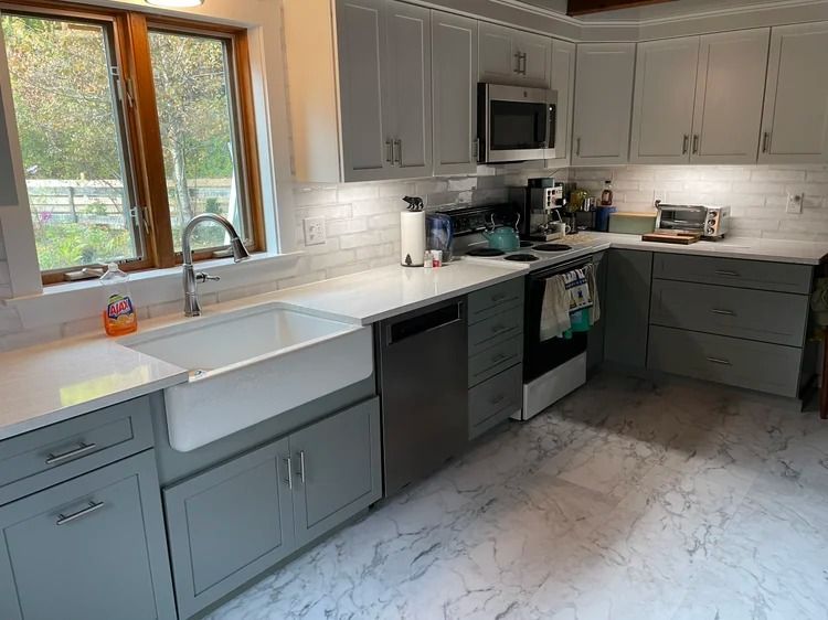 Gray and white kitchen with a farmhouse sink, stainless steel appliances, and white countertops.