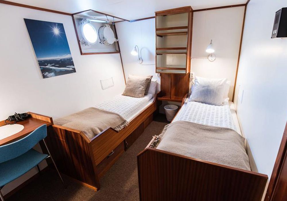 Compact bedroom with two single beds, wooden shelving, and a small desk by a window with a sea view