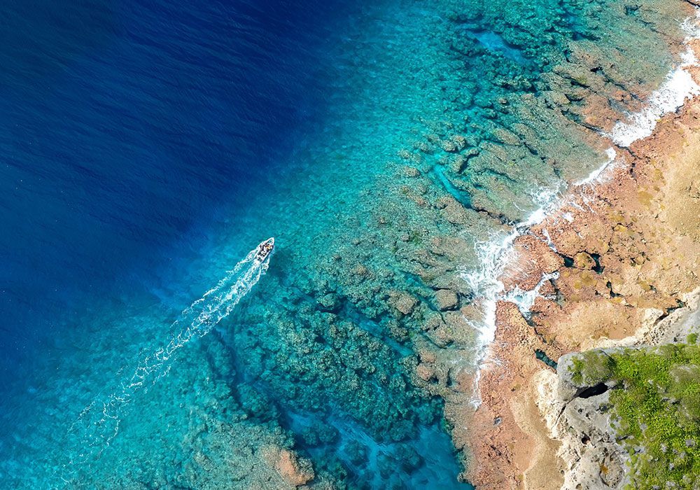 Aerial view of a boat on turquoise water near a rocky coastline and blue ocean.