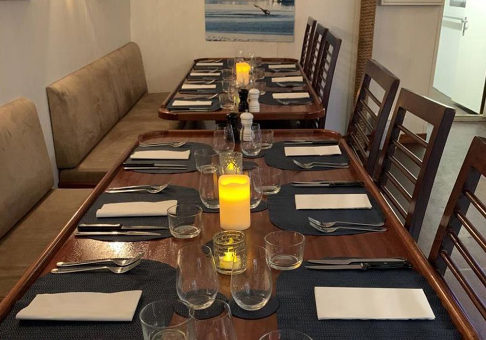 Long dining table set for a formal meal, with candles, dark placemats, and wooden chairs along both sides.