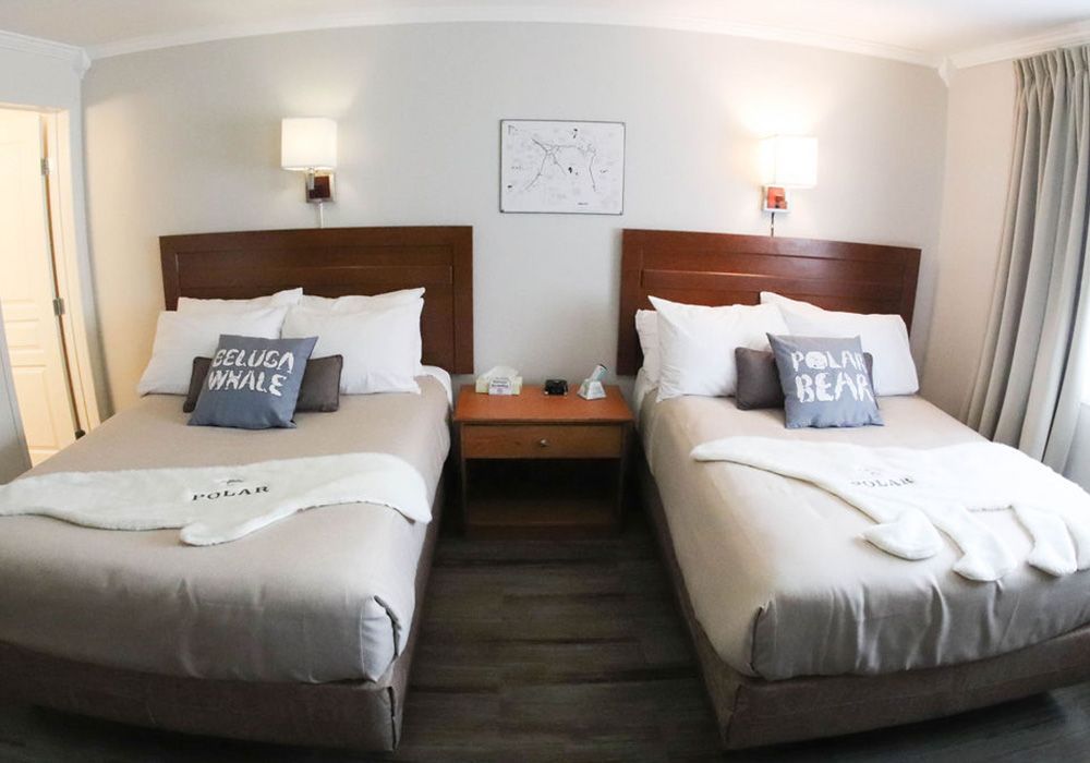 Two beds with white linens, wooden headboards, and nightstand in a hotel room.