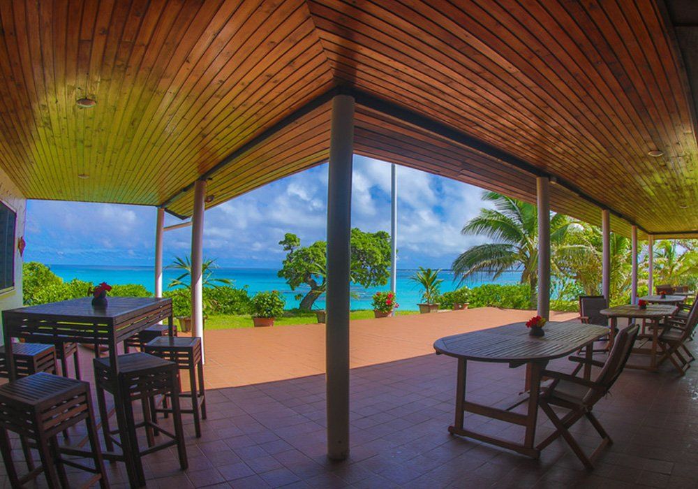 Open-air patio with tables and chairs overlooking a turquoise ocean and palm trees