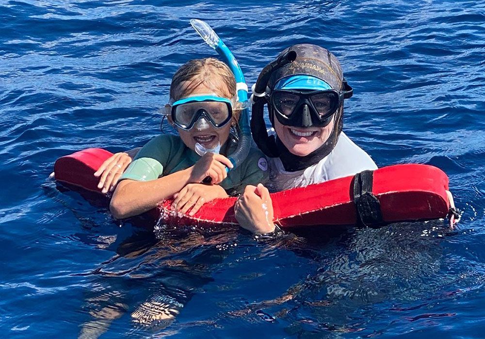 Two people in snorkel gear smiling and holding a red float in deep blue water