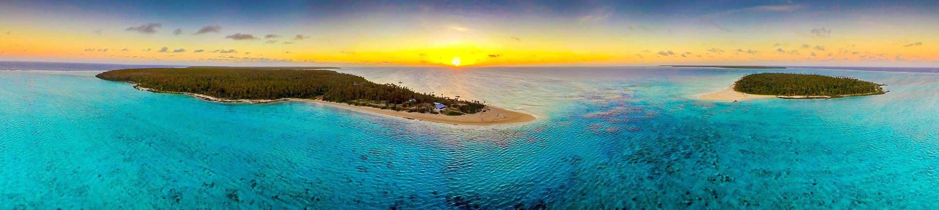 Turquoise tropical sea at sunset with small sandy islands and a yellow-orange horizon