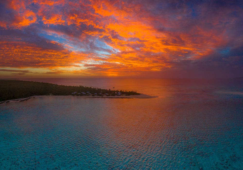 Vibrant orange sunset over a calm ocean with a dark coastline and blue water reflection