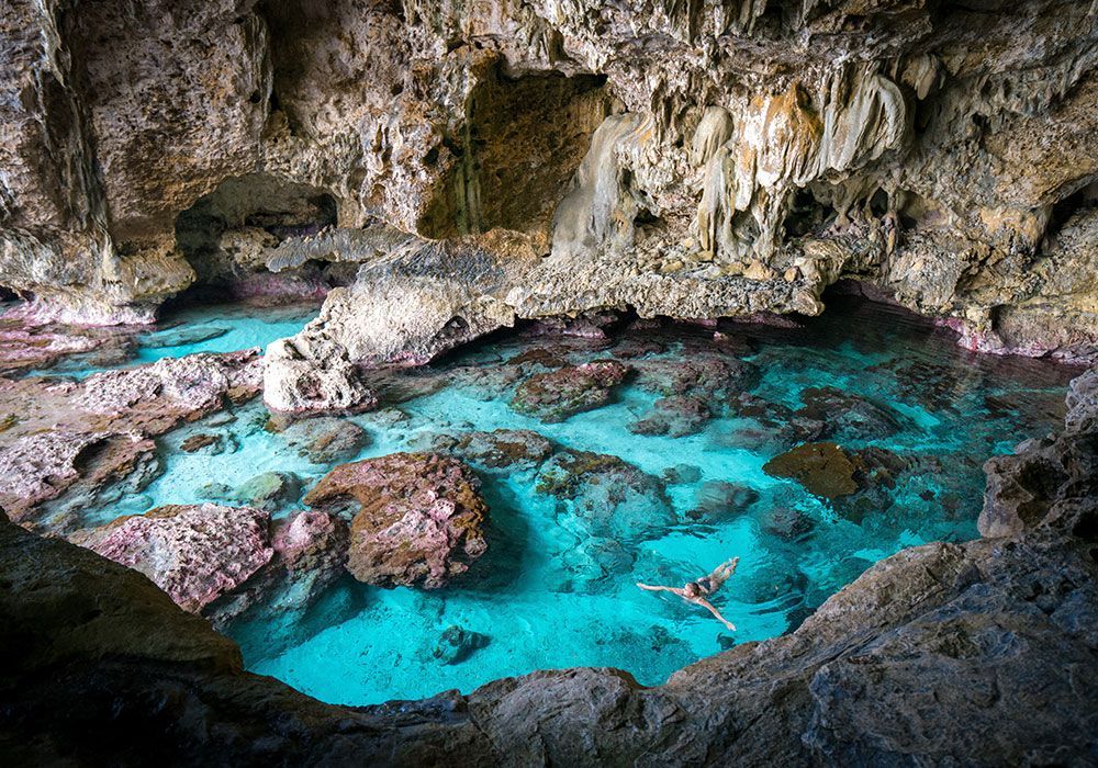 Cave pool with clear turquoise water. A person swims in the water, and the cave has rock formations.