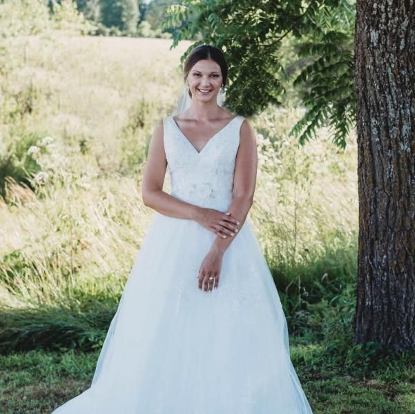 Bride in a white wedding dress standing outdoors by a tree and tall grass