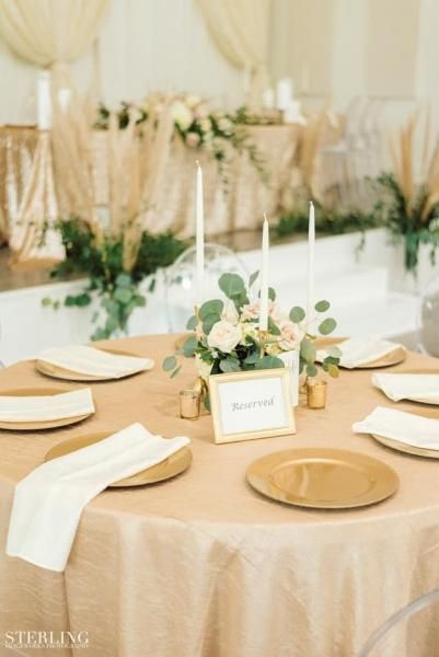 Elegant banquet table with beige linens, gold plates, and a small floral centerpiece in a bright reception hall