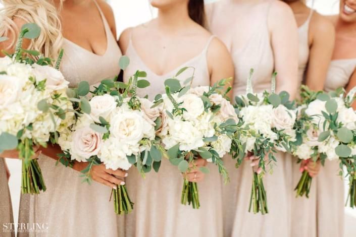 Bridesmaids in blush dresses holding white and pale pink bouquets at a wedding ceremony