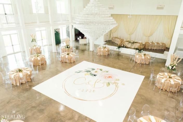 Bright, elegant banquet hall with round tables, white chairs, and a large white dance floor centerpiece