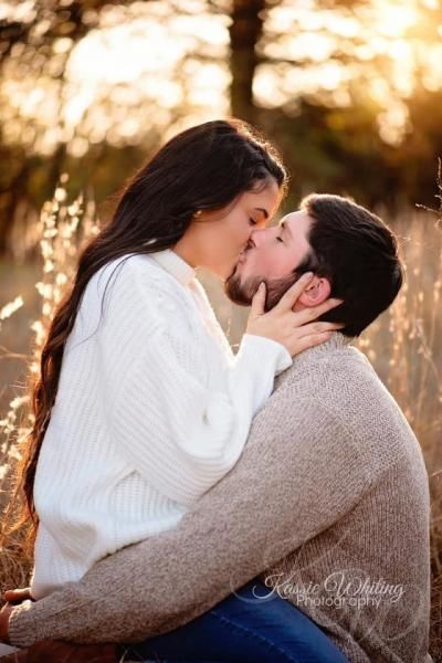 Couple embracing and kissing outdoors in warm sunset light, with bare trees in the background.