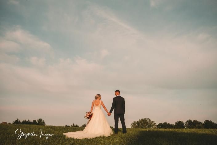 Bride and groom holding hands in a grassy field under a cloudy sky