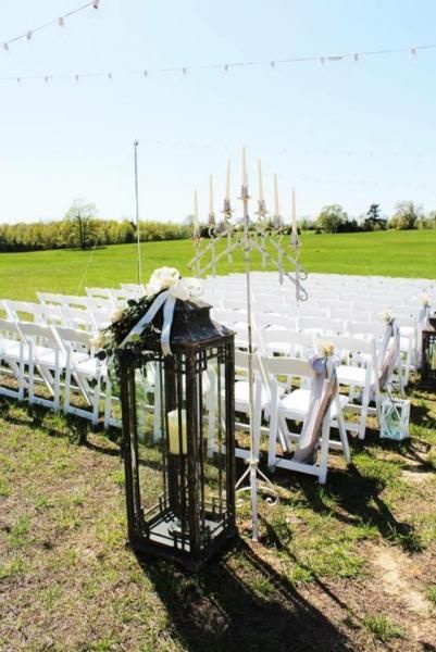 Outdoor wedding setup with white chairs and lanterns on a grassy field under a clear blue sky