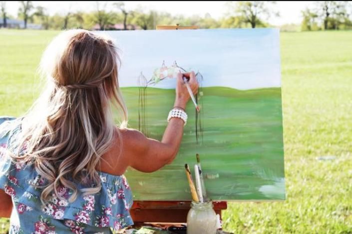 Woman painting a green landscape on a canvas outdoors in a grassy field