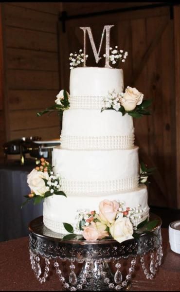 Four-tier white wedding cake with floral accents and a monogram topper on a decorative table