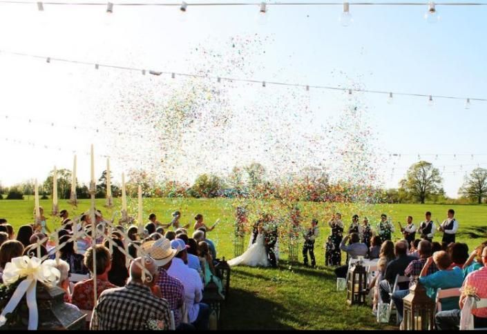 Outdoor wedding ceremony with confetti falling over seated guests and the bride and groom on a grassy lawn