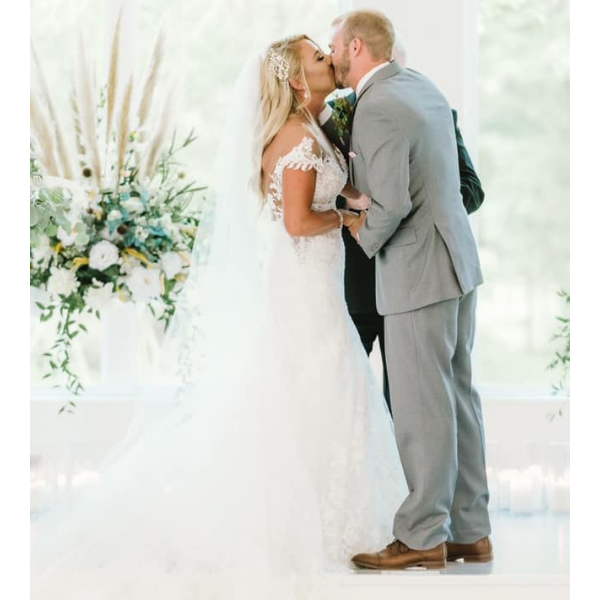 Bride and groom kissing during their wedding ceremony in a bright, white venue