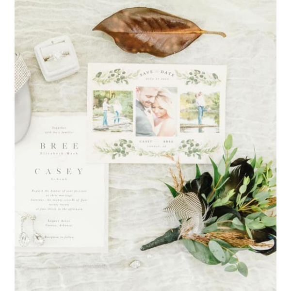 Wedding invitation suite with greenery, dried leaf, and floral arrangement on a white surface
