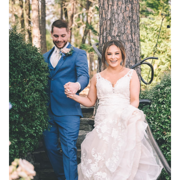 Bride and groom in blue suit and white gown descending garden steps, smiling and holding hands