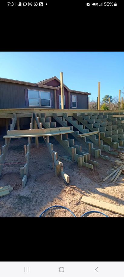 House with elevated wooden deck and stairs in a dry, rocky yard under a clear blue sky