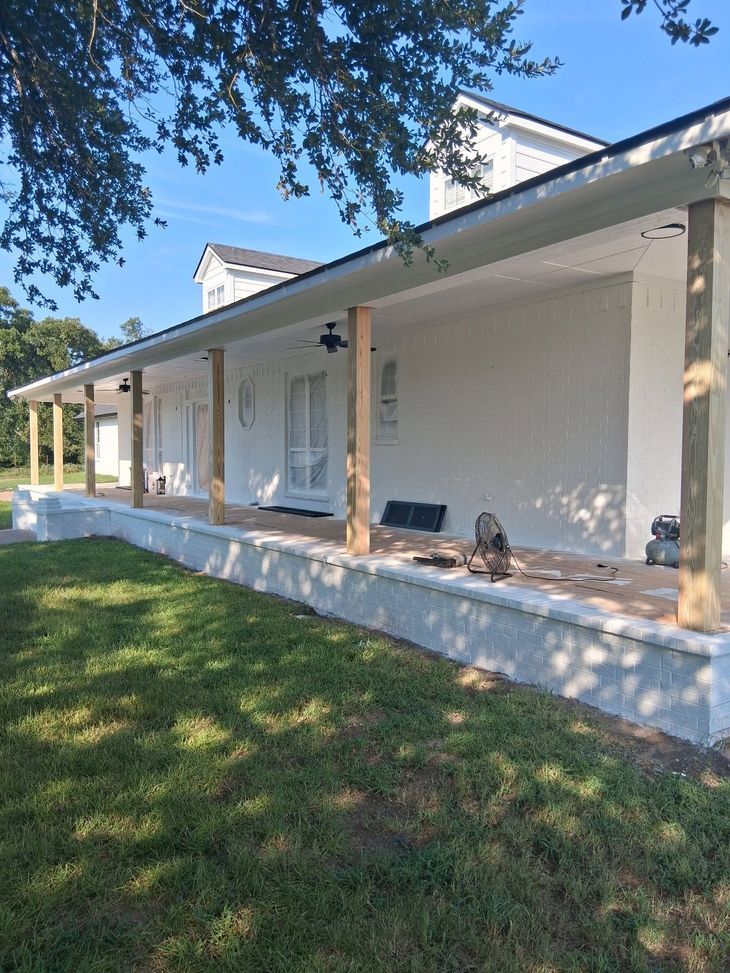 White house with a covered front porch and columns, seen from a grassy yard on a sunny day