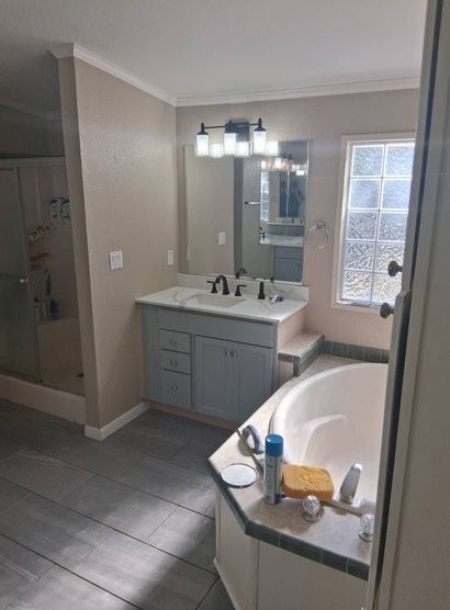 Bathroom with vanity, large mirror, and white bathtub beside a glass block window.