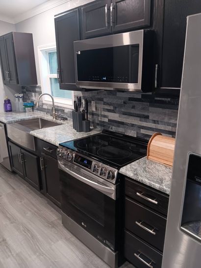 Modern kitchen with black appliances, dark cabinets, granite counters, and gray tile backsplash