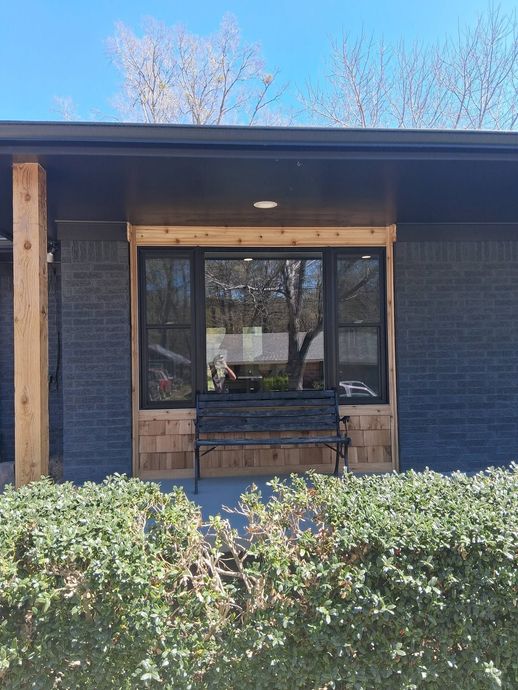 Modern building entrance with blue siding, wood trim, glass doors, and shrubs in front